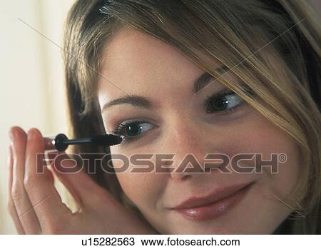 Stock Image - Young woman putting on mascara. Fotosearch