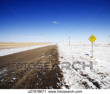Stock Image - Desolate dirt road with snow covered ground and road sign.. Fotosearch