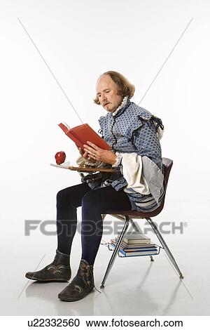 Stock Image - William Shakespeare in period clothing sitting in school desk reading a book.. Fotosearch