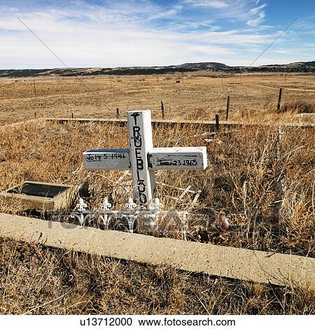 Stock Image - A cross tombstone in cemetery with landscape in background.. Fotosearch
