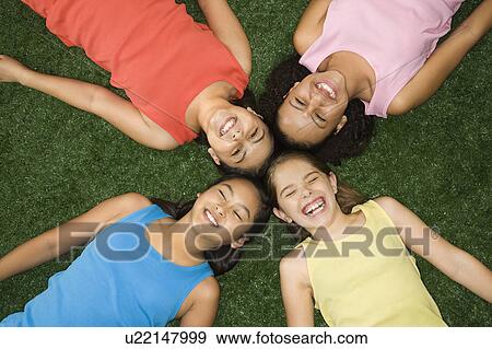 Stock Photo - Above view of four girls lying on artificial grass with heads together laughing.. Fotosearch