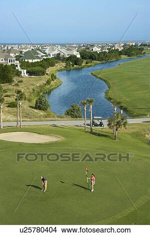 Picture - Aerial view of two people palying golf near residential community at Bald Head Island, North Carolina.. Fotosearch