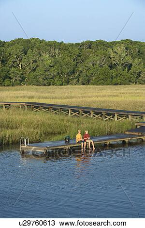 Stock Image - Aerial view of two teenage boys fishing from dock in marshy lowlands of Bald Head Island, North Carolina.. Fotosearch