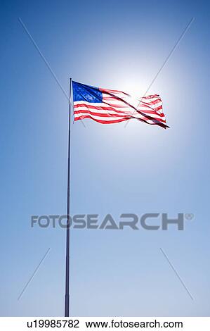 Stock Image - American flag blowing in clear blue sky.. Fotosearch