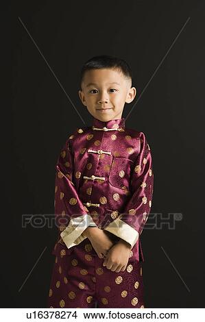 Picture - Asian boy in traditional attire standing against black background.. Fotosearch