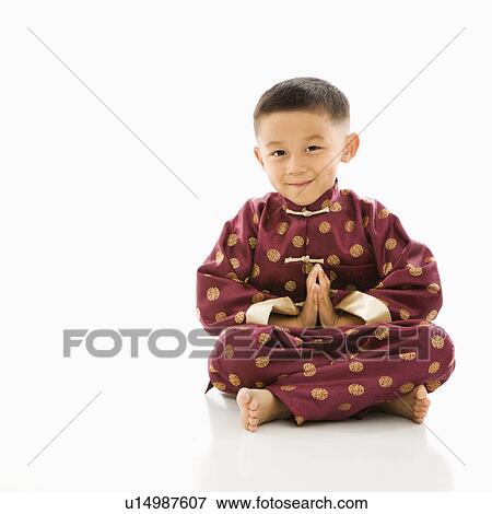 Stock Photo - Asian boy sitting meditating against white background in traditional attire.. Fotosearch