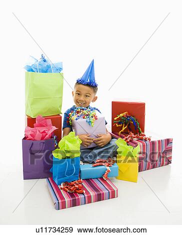 Asian boy wearing party hat sitting with pile of wrapped presents. View Large Photo Image Stock Photo - Asian boy wearing party hat sitting with pile of wrapped presents.. Fotosearch