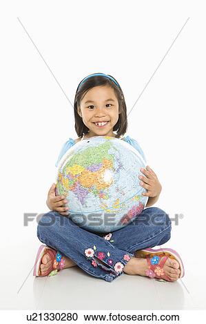Stock Image - Asian girl sitting on floor holding Earth globe in her lap.. Fotosearch
