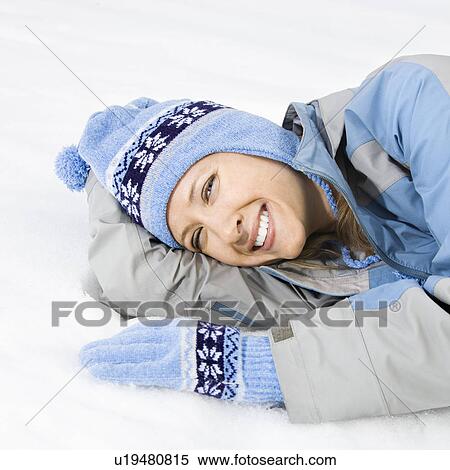 Stock Photography - Attractive smiling mid adult Caucasian woman wearing blue ski clothing lying in snow looking at viewer.. Fotosearch