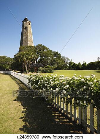 Stock Image - Bald Head Lighthouse with fence and wild roses at Bald Head Island, North Carolina.. Fotosearch