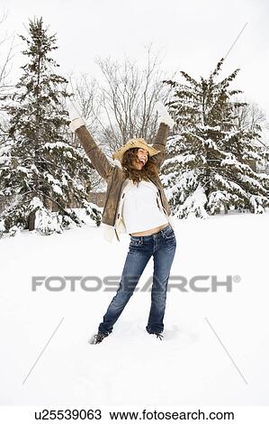 Stock Image - Carefree Caucasian young adult female standing with arms above head in snow wearing straw cowboy hat.. Fotosearch