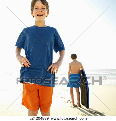 Caucasian boy with hands on hips with another Caucasian boy with bodyboard in background. View Large Photo Image Stock Photo - Caucasian boy with hands on hips with another Caucasian boy with bodyboard in background.. Fotosearch