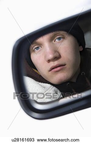 Stock Image - Caucasian male teenager looking at himself in side view mirror of car.. Fotosearch