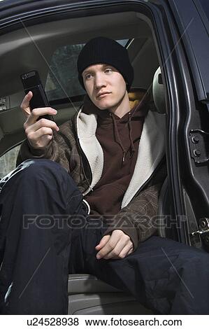 Caucasian male teenager sitting in car looking at cellphone. View Large Photo Image Stock Photo - Caucasian male teenager sitting in car looking at cellphone.. Fotosearch