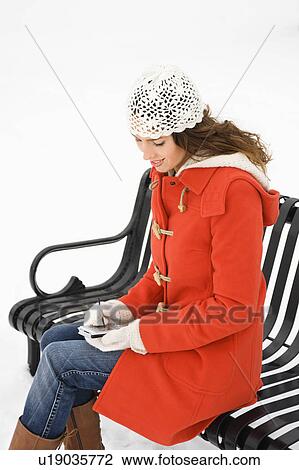 Stock Image - Caucasian young adult female sitting on park bench using PDA.. Fotosearch
