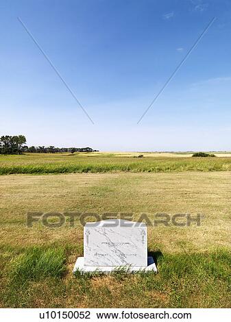 Stock Image - Cemetary headstone in rural field under blue sky.. Fotosearch