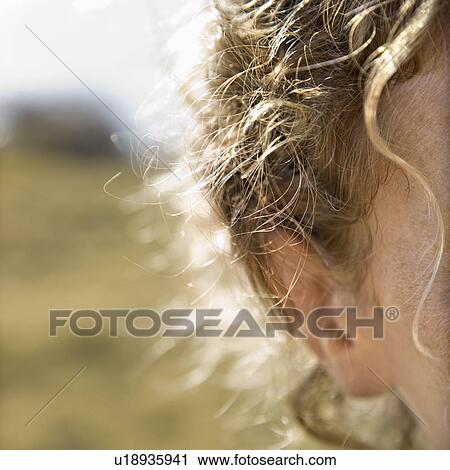 Stock Image - Close up of Caucasian mid-adult female forehead and ear with wavy hair.. Fotosearch