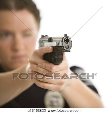 Stock Image - Close up of mid adult female Caucasian law enforcement officer aiming gun at viewer with one eye closed.. Fotosearch