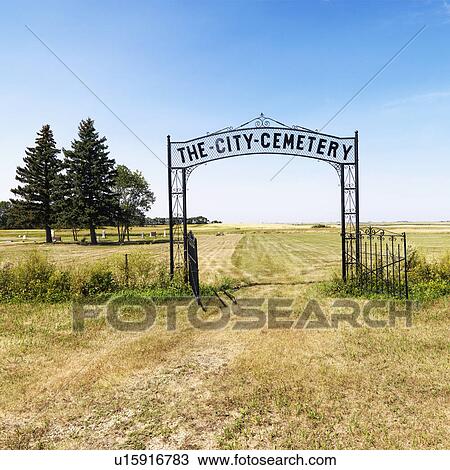 Stock Image - Entrance to rural cemetary in field with decorative iron gate.. Fotosearch
