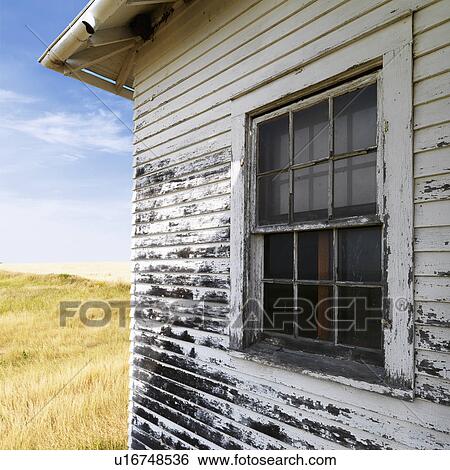 Stock Photograph - Exterior of weathered abandoned building with peeling paint and window in grassland.. Fotosearch