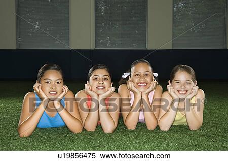 Four multiethnic girls lying on ground in indoor gym with heads on hands smiling. View Large Photo Image Stock Photography - Four multiethnic girls lying on ground in indoor gym with heads on hands smiling.. Fotosearch