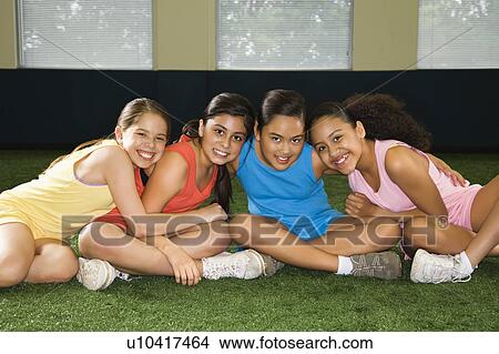 Four multiethnic girls sitting with arms around eachother smiling. View Large Photo Image Picture - Four multiethnic girls sitting with arms around eachother smiling.. Fotosearch