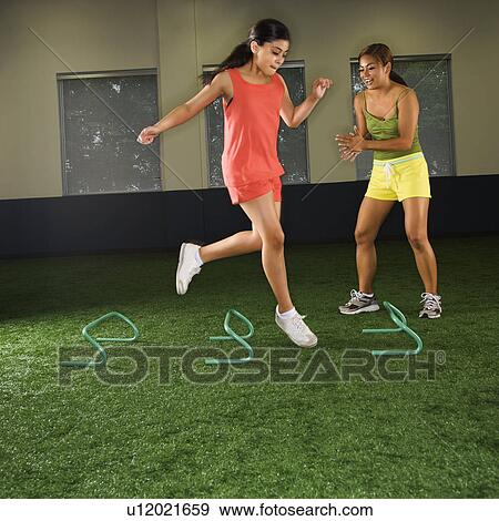 Girl jumping step hurdles in indoor gym while woman coach watches. View Large Photo Image Stock Photo - Girl jumping step hurdles in indoor gym while woman coach watches.. Fotosearch
