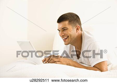 Handsome Caucasian mid adult man lying in bed with laptop. View Large Photo Image Stock Image - Handsome Caucasian mid adult man lying in bed with laptop.. Fotosearch