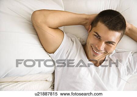Stock Photography - High angle view of handsome Caucasian mid adult man lying with hands behind head smiling.. Fotosearch