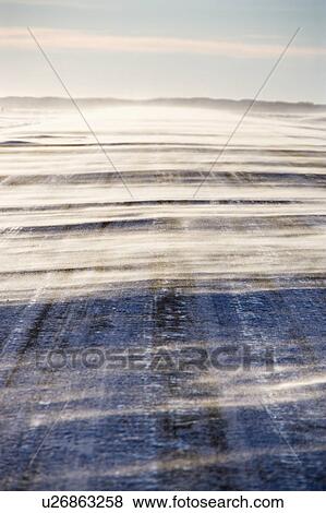 Stock Photo - Ice covered road with snow being blown over.. Fotosearch