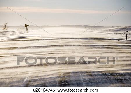 Stock Photography - Ice covered road with snow being blown over.. Fotosearch