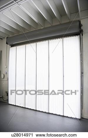 Stock Image - Interior of warehouse building with large window and vertical blinds.. Fotosearch