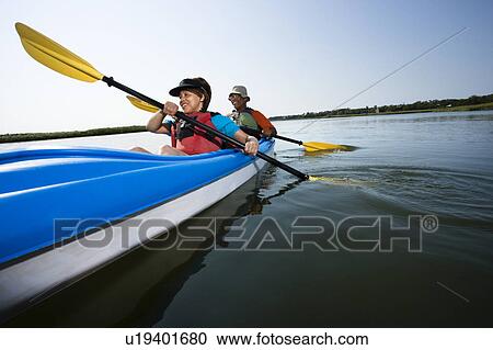 Stock Image - Low angle of African American middle-aged man and woman paddling kayak.. Fotosearch