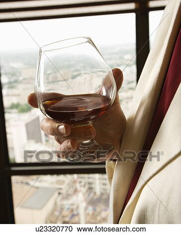 Stock Image - Man in suit holding snifter of brandy.. Fotosearch