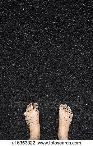 Stock Image - Man's barefeet in black sand in Maui Hawaii. Fotosearch