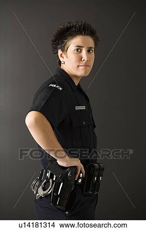 Picture - Portrait of mid adult Caucasian policewoman standing with hand on gun holster looking at viewer.. Fotosearch