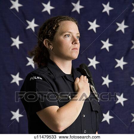 Stock Image - Portrait of mid adult Caucasian policewoman pledging allegiance with American flag as backdrop.. Fotosearch