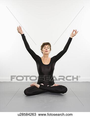 Stock Image - Portrait of pretty Caucasian woman in spandex bodysuit sitting in meditation pose with arms raised.. Fotosearch