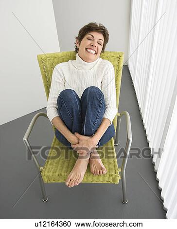 Stock Image - Portrait of pretty Caucasian woman smiling sitting on modern chair.. Fotosearch