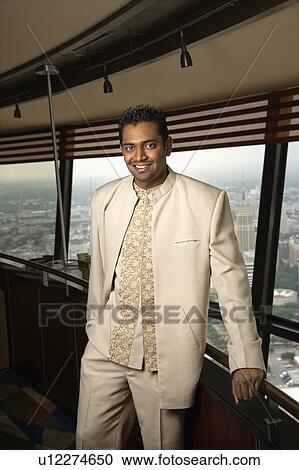 Portrait of young adult male Indian standing near window in tower restaurant smiling at viewer. View Large Photo Image Stock Image - Portrait of young adult male Indian standing near window in tower restaurant smiling at viewer.. Fotosearch