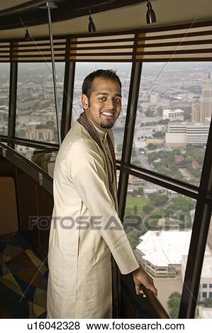 Portrait of young adult male Indian standing near window in tower restaurant smiling at viewer. View Large Photo Image Stock Photo - Portrait of young adult male Indian standing near window in tower restaurant smiling at viewer.. Fotosearch
