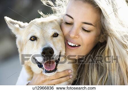 Stock Photograph - Pretty Caucasian blond woman hugging brown dog and smiling.. Fotosearch