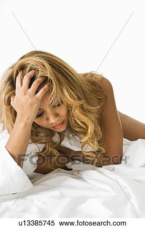 Stock Photography - Pretty woman lying on bed holding hand to head looking stressed.. Fotosearch