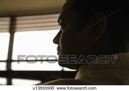 Stock Image - Profile view of young adult male Indian slihouetted near window.. Fotosearch