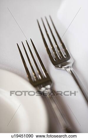 Stock Image - Salad fork and dinner fork with plate on white table cloth.. Fotosearch