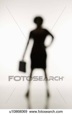 Stock Photo - Soft focus silhouette of businesswoman standing with hand on hip holding briefcase.. Fotosearch