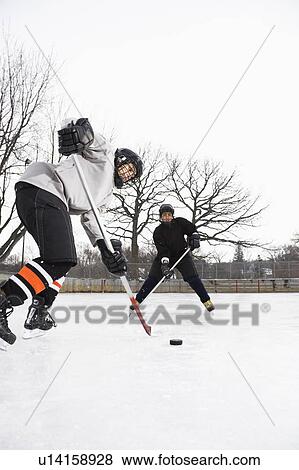 Stock Photo - Two boys in ice hockey uniforms skating on ice rink moving puck.. Fotosearch