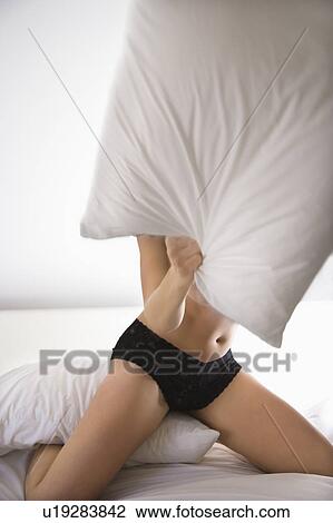 Stock Image - Woman kneeling on bed in black lace panties pillow fighting.. Fotosearch