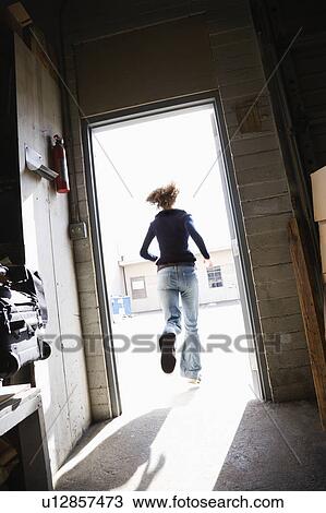 Stock Image - Woman running through open door from building to sunny outside.. Fotosearch