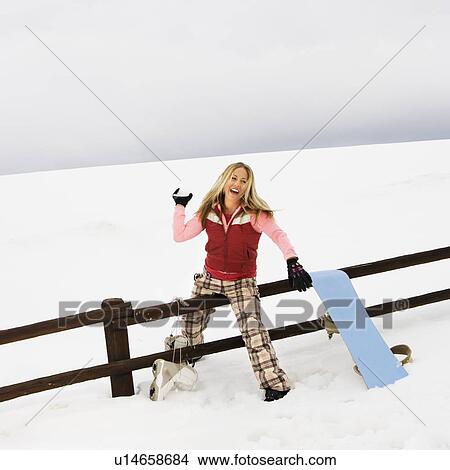 Young woman in winter clothes by fence in snowy field smiling while ready to throw snowball. View Large Photo Image Picture - Young woman in winter clothes by fence in snowy field smiling while ready to throw snowball.. Fotosearch